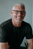 Headshot of Marc Berry, co-founder of Sage, smiling in glasses and a black t-shirt against a light gray studio backdrop